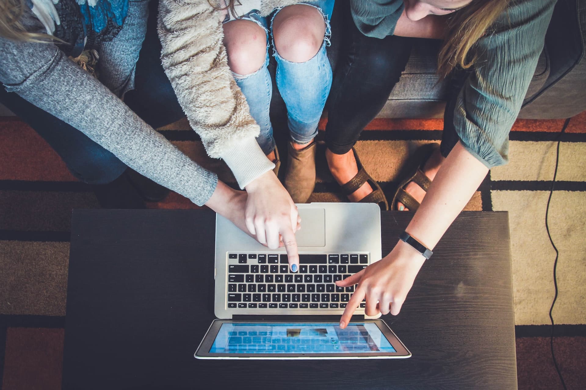 three people pointing towards a laptop screen and keyboard, working together