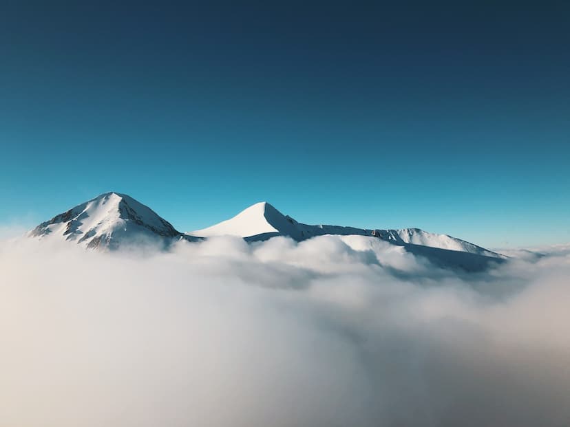 Snowy Mountain Peaks above a sea of clouds on a clear blue sky