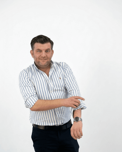 Ein Mann in gestreiftem Hemd lächelt und krempelt seinen Ärmel hoch.