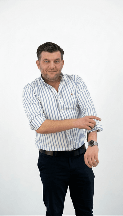 Ein Mann in gestreiftem Hemd lächelt und krempelt seinen Ärmel hoch.