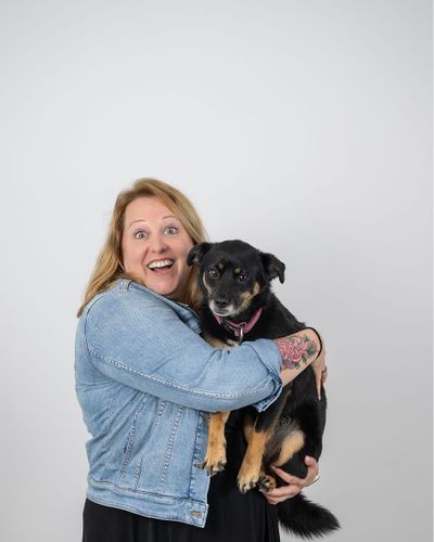 Frau mit lächelndem Ausdruck hält einen kleinen schwarz-braunen Hund im Arm.