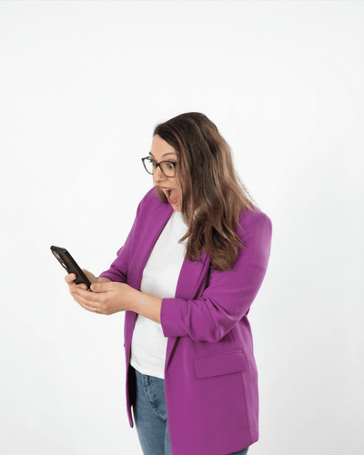 Frau in lila Blazer schaut überrascht auf ihr Smartphone.
