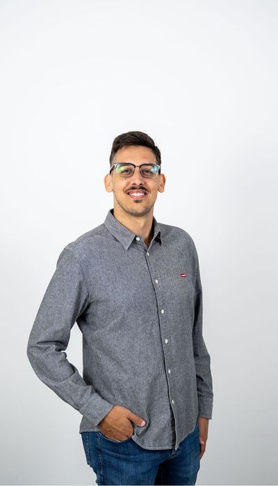 Mann mit Brille und grauem Hemd lächelt freundlich in die Kamera.