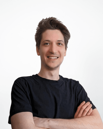 Person in schwarzem T-Shirt lächelt mit verschränkten Armen vor einem neutralen Hintergrund.