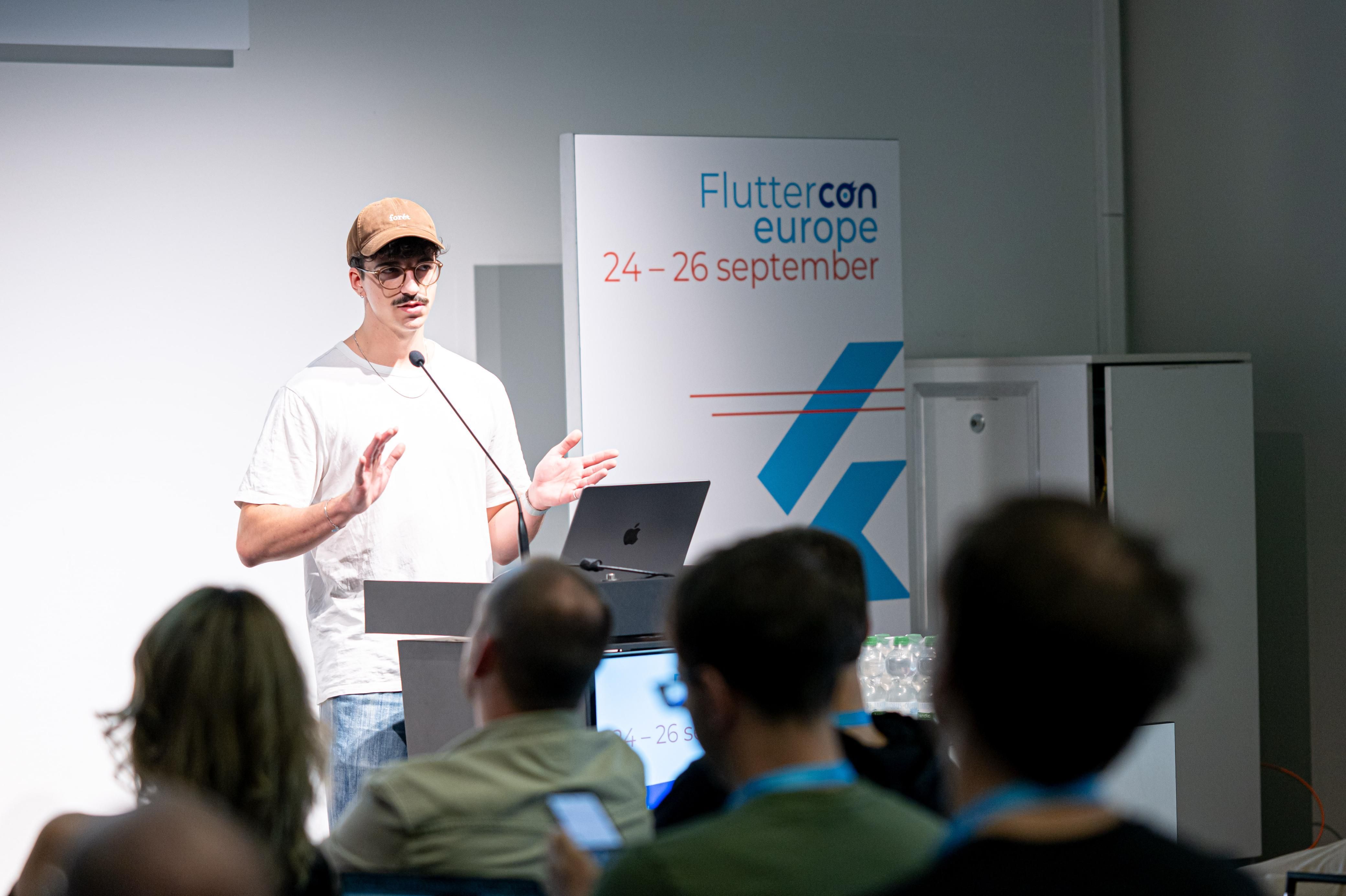 Redner gibt eine Präsentation auf der Fluttercon Europe vor einem Publikum, neben einem Schild mit dem Datum der Veranstaltung.