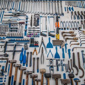 Verschiedene Werkzeuge ordentlich auf einer Wand angeordnet, darunter Schraubenschlüssel, Zangen, Hammer und Sägeblätter.