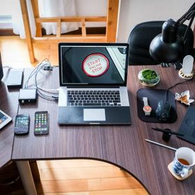Moderner Schreibtisch mit verschiedenen Elektronikgeräten, darunter ein Laptop, mehrere Smartphones, ein Tablet und Kopfhörer, sowie Bürozubehör wie eine Schreibtischlampe und eine Tasse Tee.