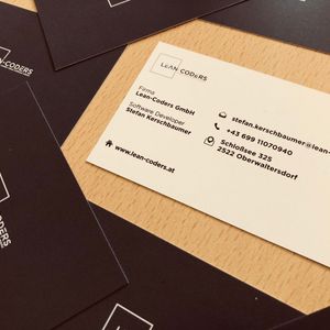 Visitenkarte von Lean-Coders mit Kontaktinformationen auf einem Tisch, umgeben von schwarzen Visitenkarten mit Unternehmenslogo.