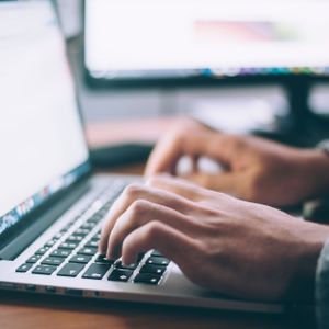 Hände tippen auf einer Laptop-Tastatur, mit verschwommenem Bildschirm im Hintergrund.