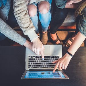 Drei Personen sitzen auf einem Sofa und zeigen gemeinsam auf den Bildschirm eines Laptops.