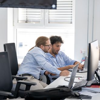 Zwei Männer in einem Büro arbeiten gemeinsam an einem Computerbildschirm.