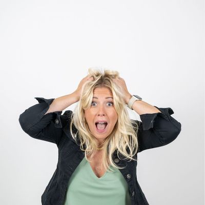 Person schaut überrascht mit offenen Mund und Händen am Kopf, überwältigt vor weißem Hintergrund.
