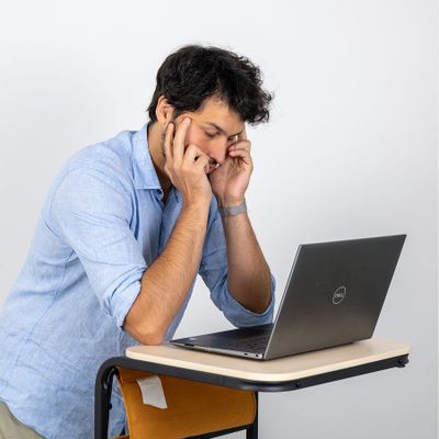 Person in hellblauem Hemd stützt sich nachdenklich auf einem Stehpult mit einem Laptop ab und blickt auf den Bildschirm.