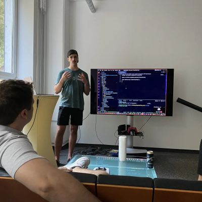 Junger Mann präsentiert Programmiercode auf einem Bildschirm vor einer kleinen Gruppe in einem Besprechungsraum.