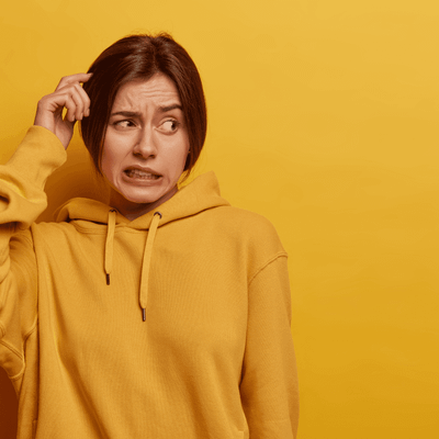 Person in einem gelben Hoodie schaut verwirrt und kratzt sich am Kopf, vor einem einfarbig gelben Hintergrund.