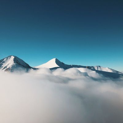 Schneebedeckte Berggipfel ragen über eine Wolkendecke in strahlend blauem Himmel hinaus.
