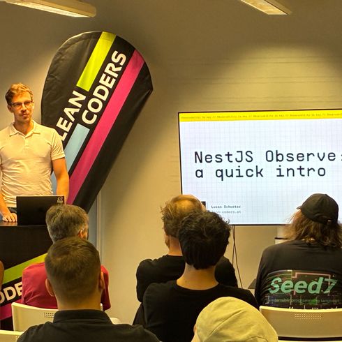 Junger Mann in einem weißen Poloshirt steht an einem Rednerpult und präsentiert vor einem Bildschirm, der den Titel „NestJS Observe: a quick intro“ zeigt. Im Hintergrund sind mehrere Zuhörer sichtbar, teilweise mit verschiedenen Frisuren und Bekleidungen, die aufmerksam zuhören. Das Banner im Hintergrund trägt die Aufschrift „LEAN CODERS“.