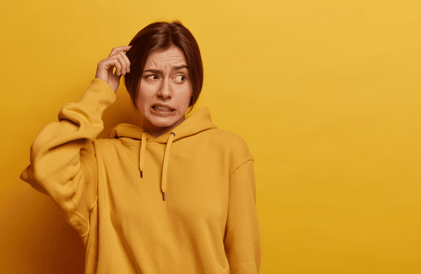 Person in einem gelben Hoodie schaut verwirrt und kratzt sich am Kopf, vor einem einfarbig gelben Hintergrund.